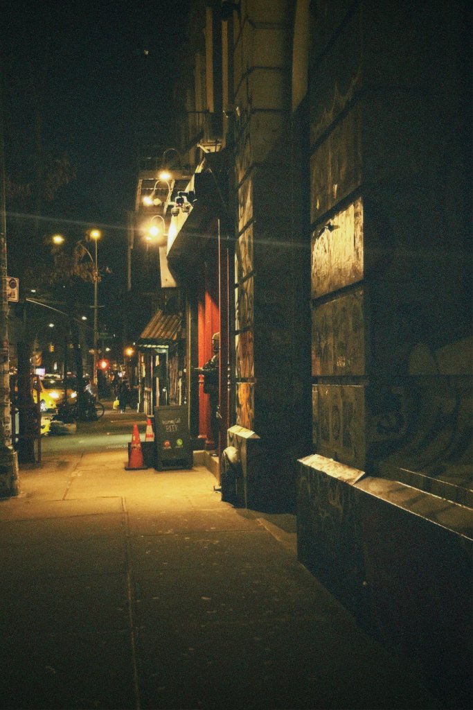 A warm-lit urban alley at night with vintage storefronts, street lamps, and fire hydrants casting golden yellow tones on the pavement