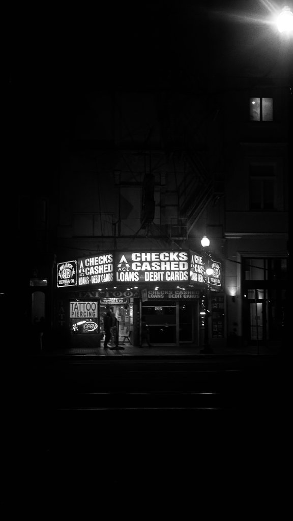 A checks cashed and tattoo parlor lit up at night on a dark New Orleans street corner