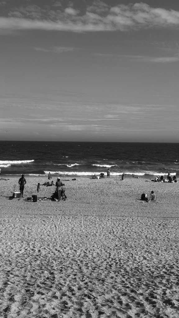 Black and white beach — scattered figures on the sand, waves breaking in the distance