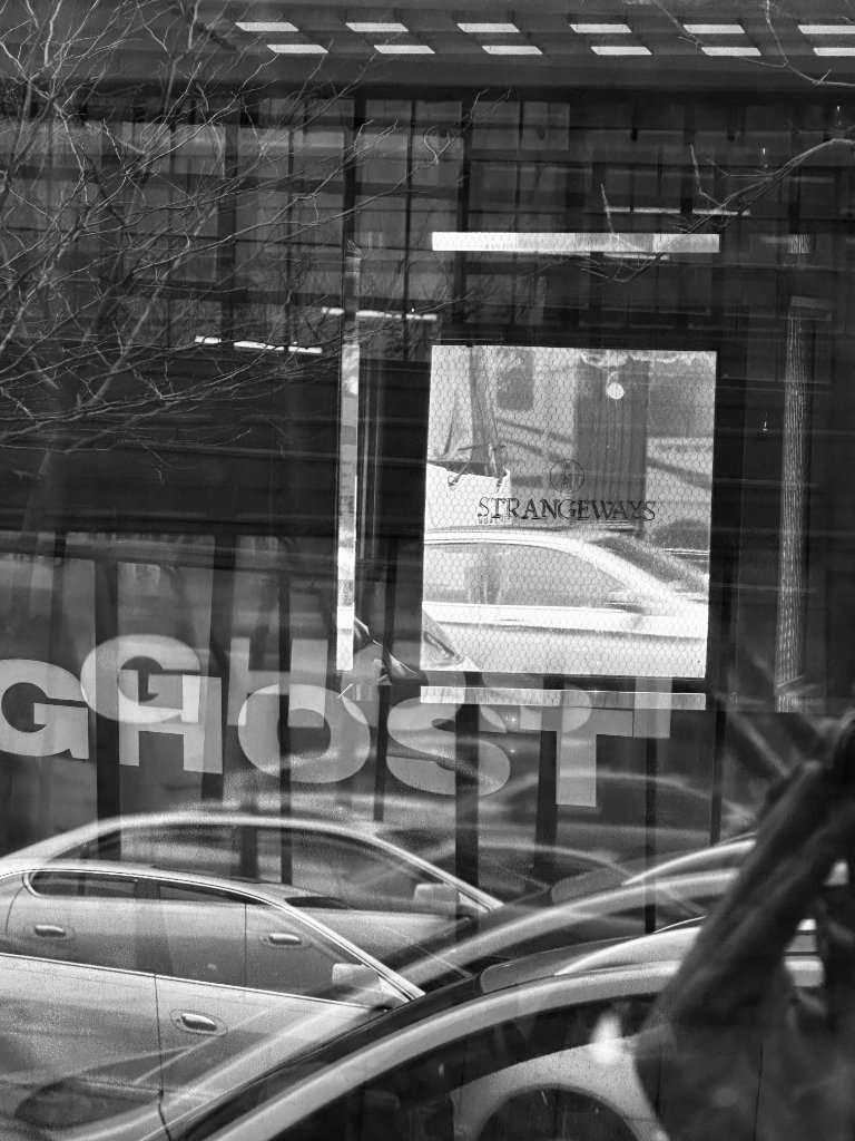 Layered window reflection — GHOST text overlaid on cars and a Strangeways sign