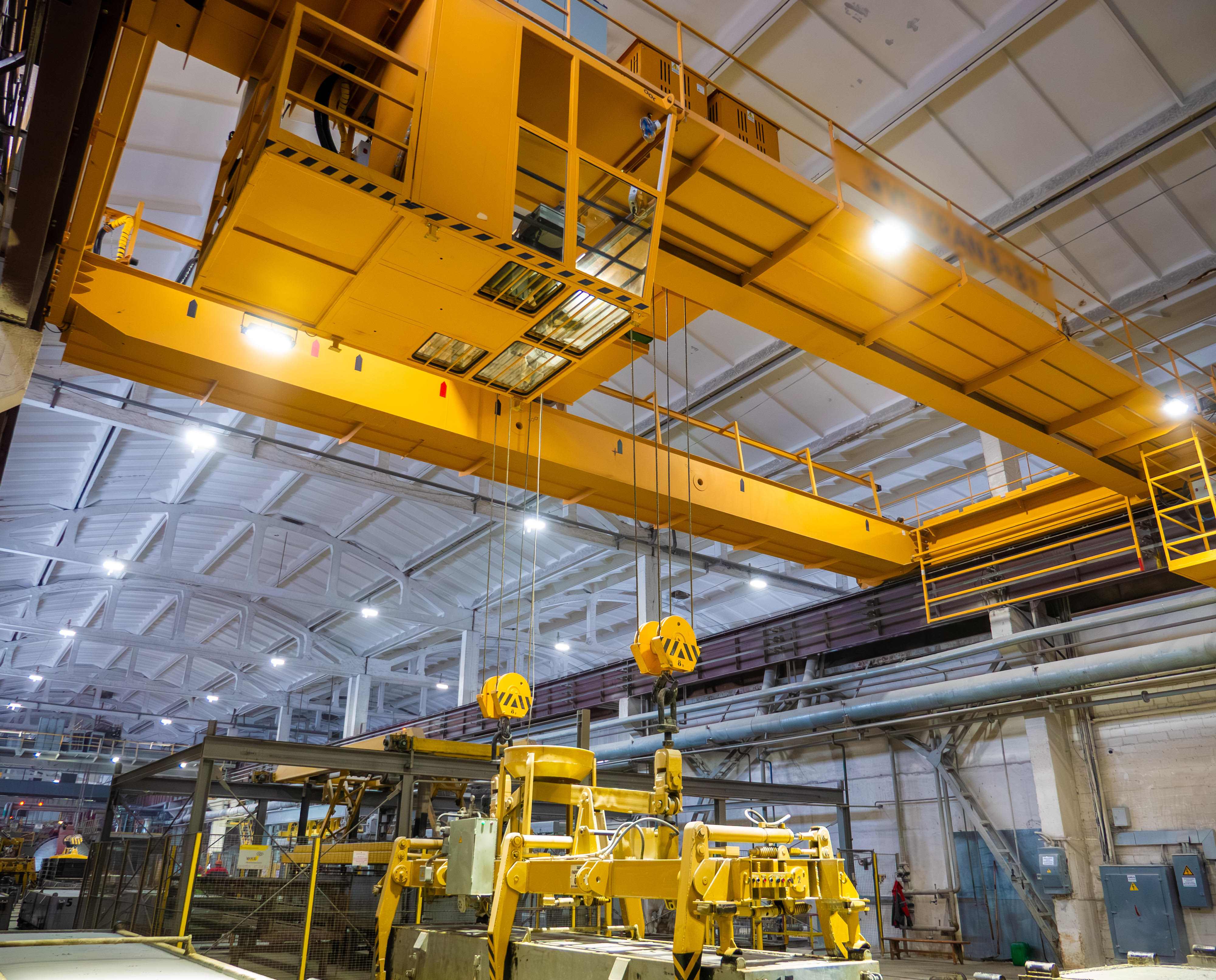 Bright-yellow overhead bridge crane with suspended hook assemblies above a factory floor