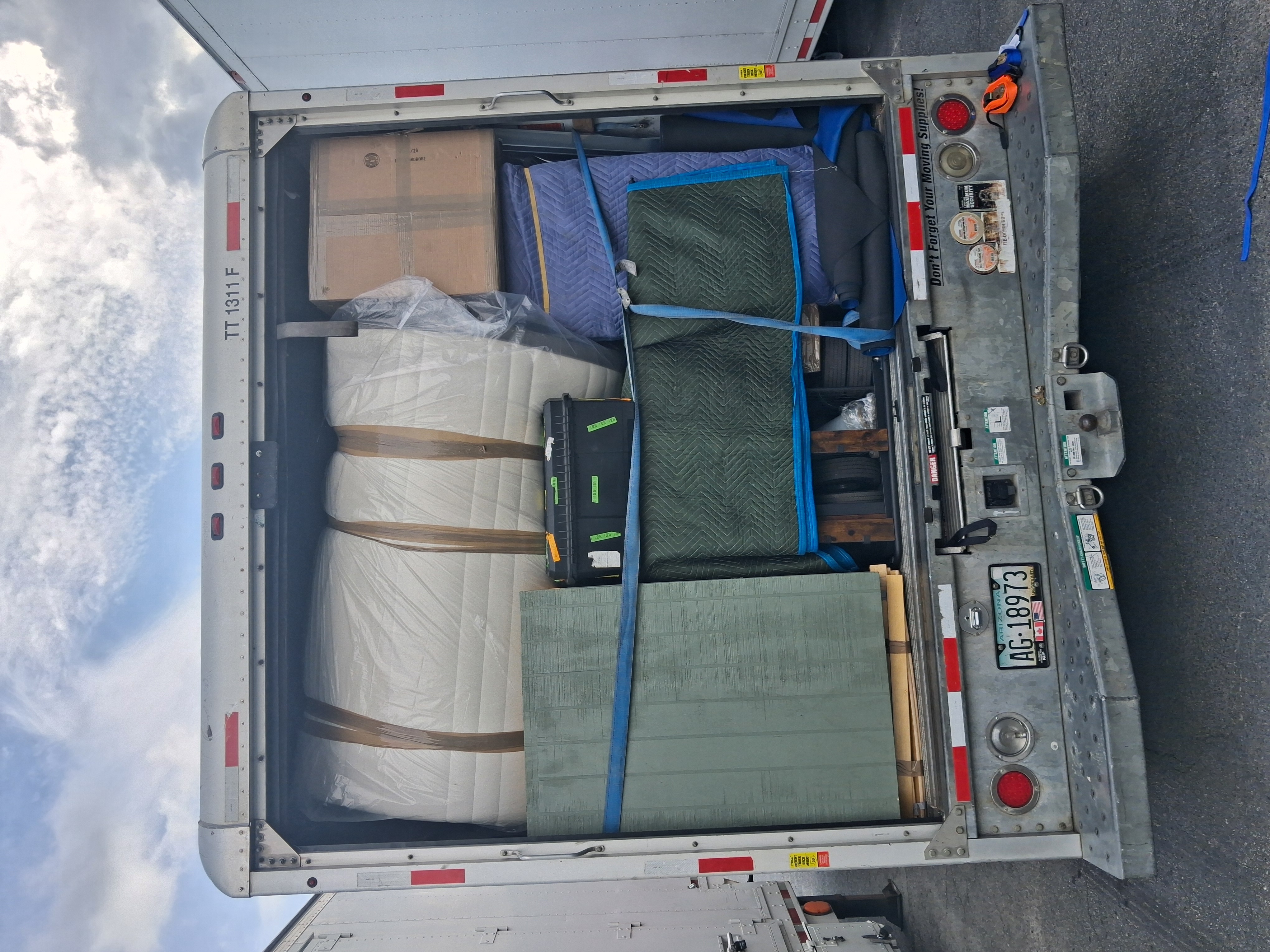 Open moving truck tightly loaded with wrapped furniture, blankets, and strapped-in items