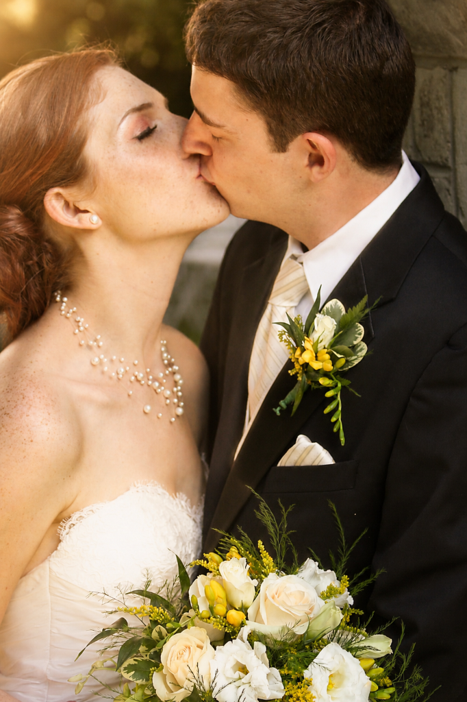 Bride and groom kissing, golden hour portrait with bouquet