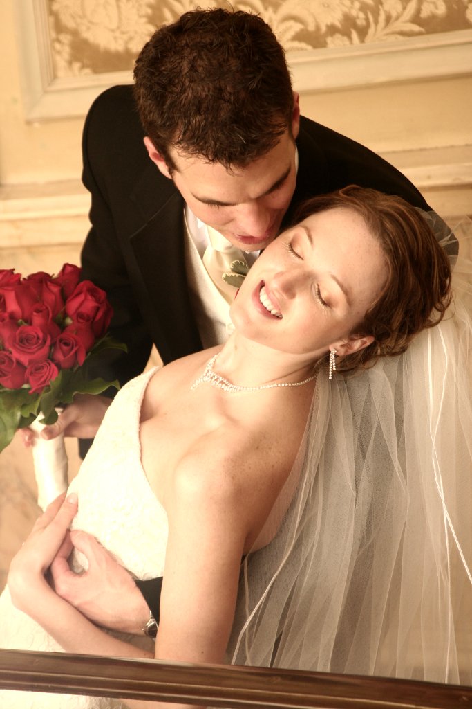 Groom whispering to laughing bride with red roses, intimate portrait