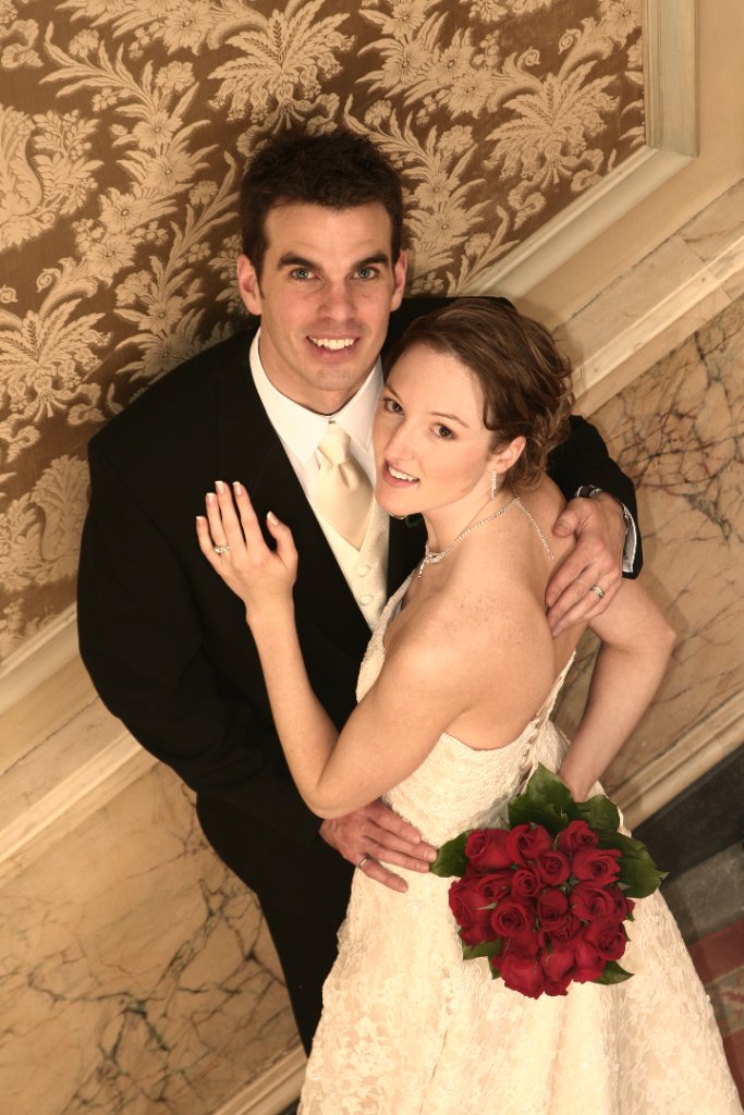 Bride and groom smiling together on staircase with red bouquet