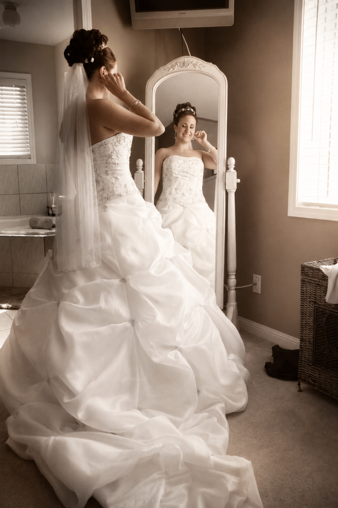 Bride adjusting her veil in an ornate standing mirror