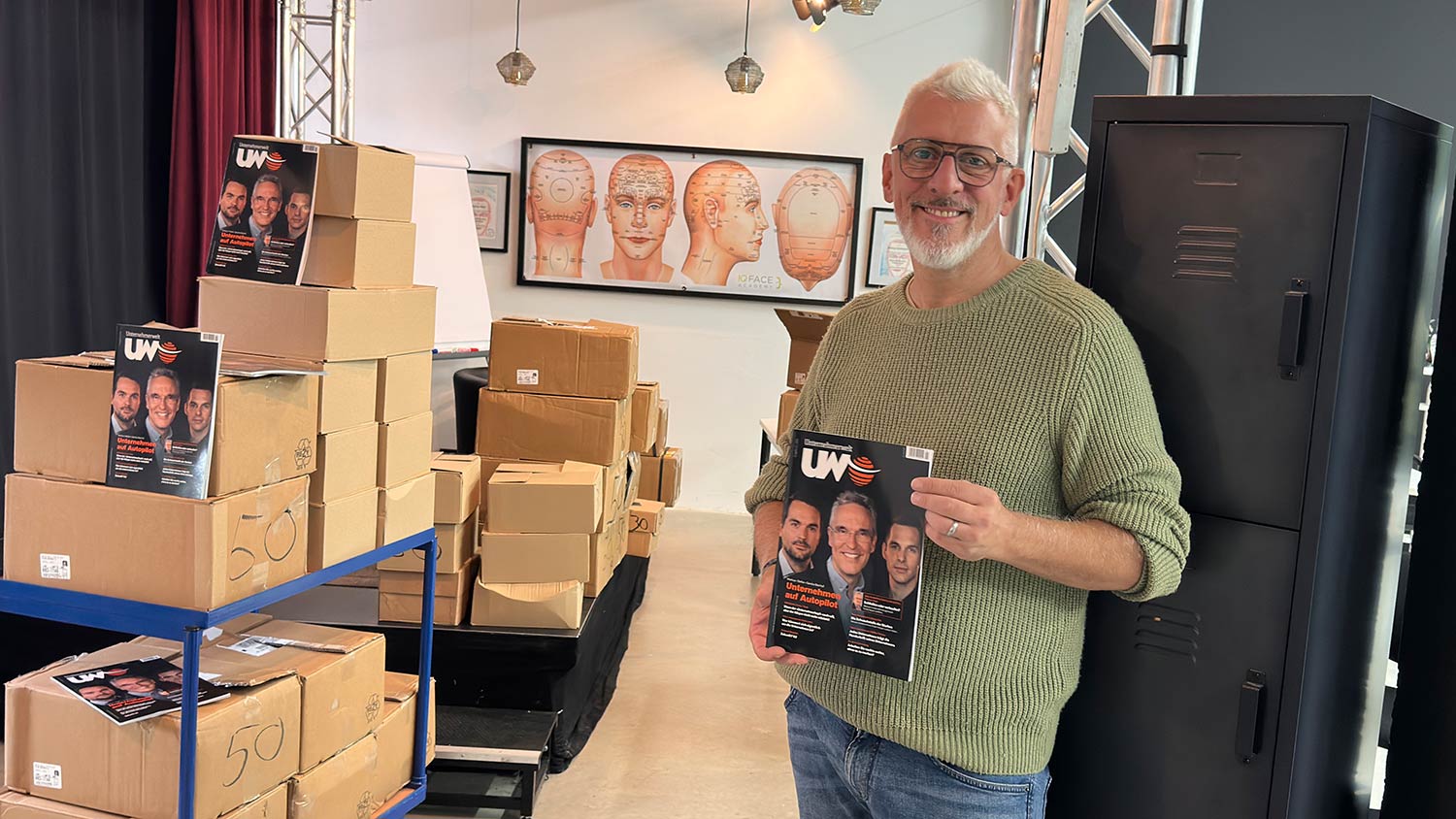 Unternehmer hält die neue Unternehmerwelt Ausgabe in der Hand, daneben Kartons mit Magazinen für den Versand an Flughäfen und Bahnhöfe