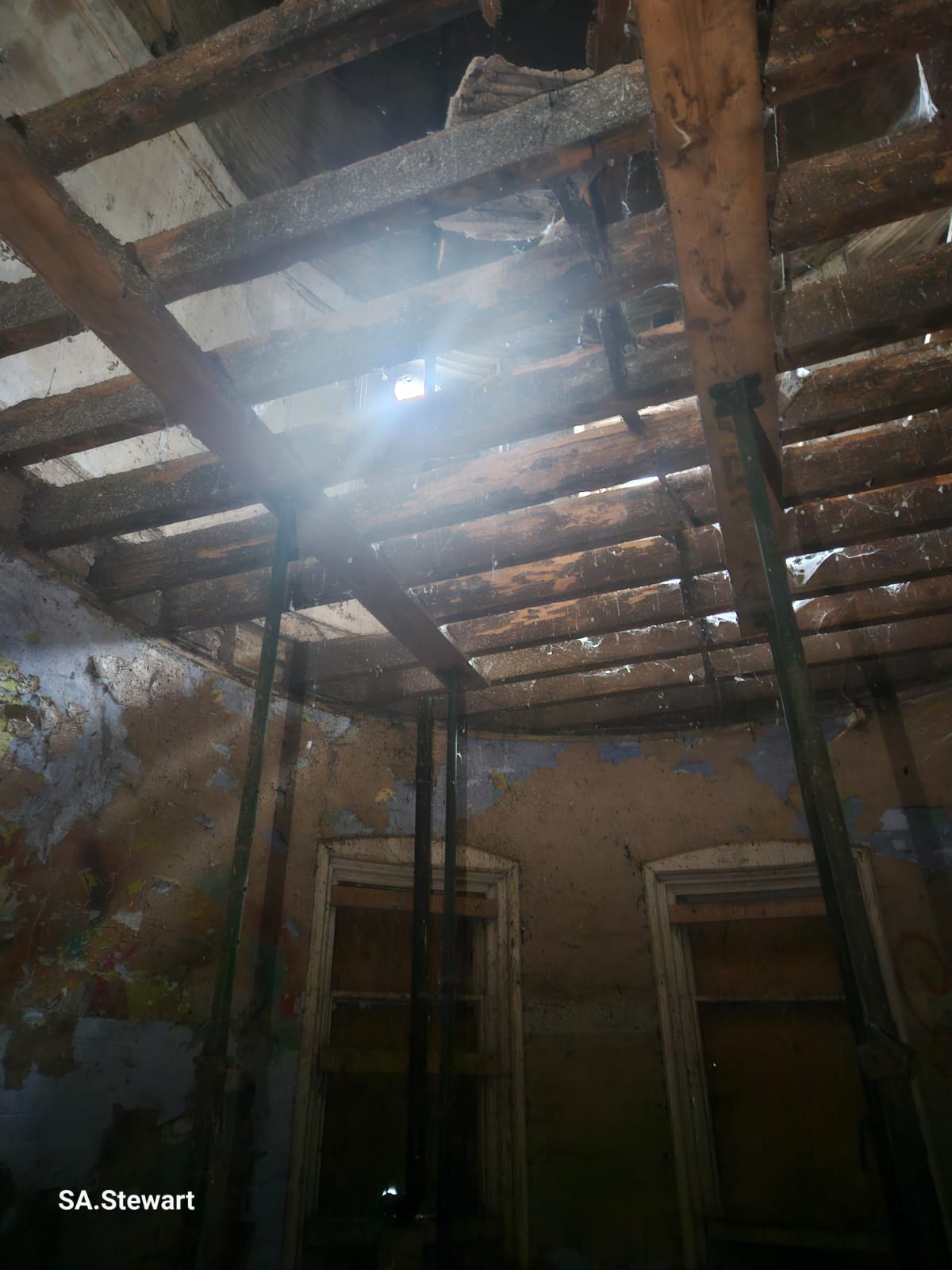 A room with a partially collapsed roof, light streaming through the gaps above