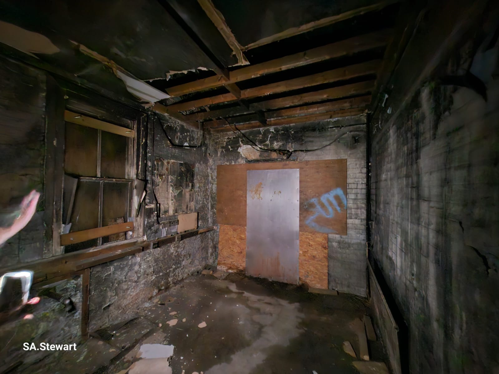 An interior room with exposed brick and a boarded doorway, showing years of decay