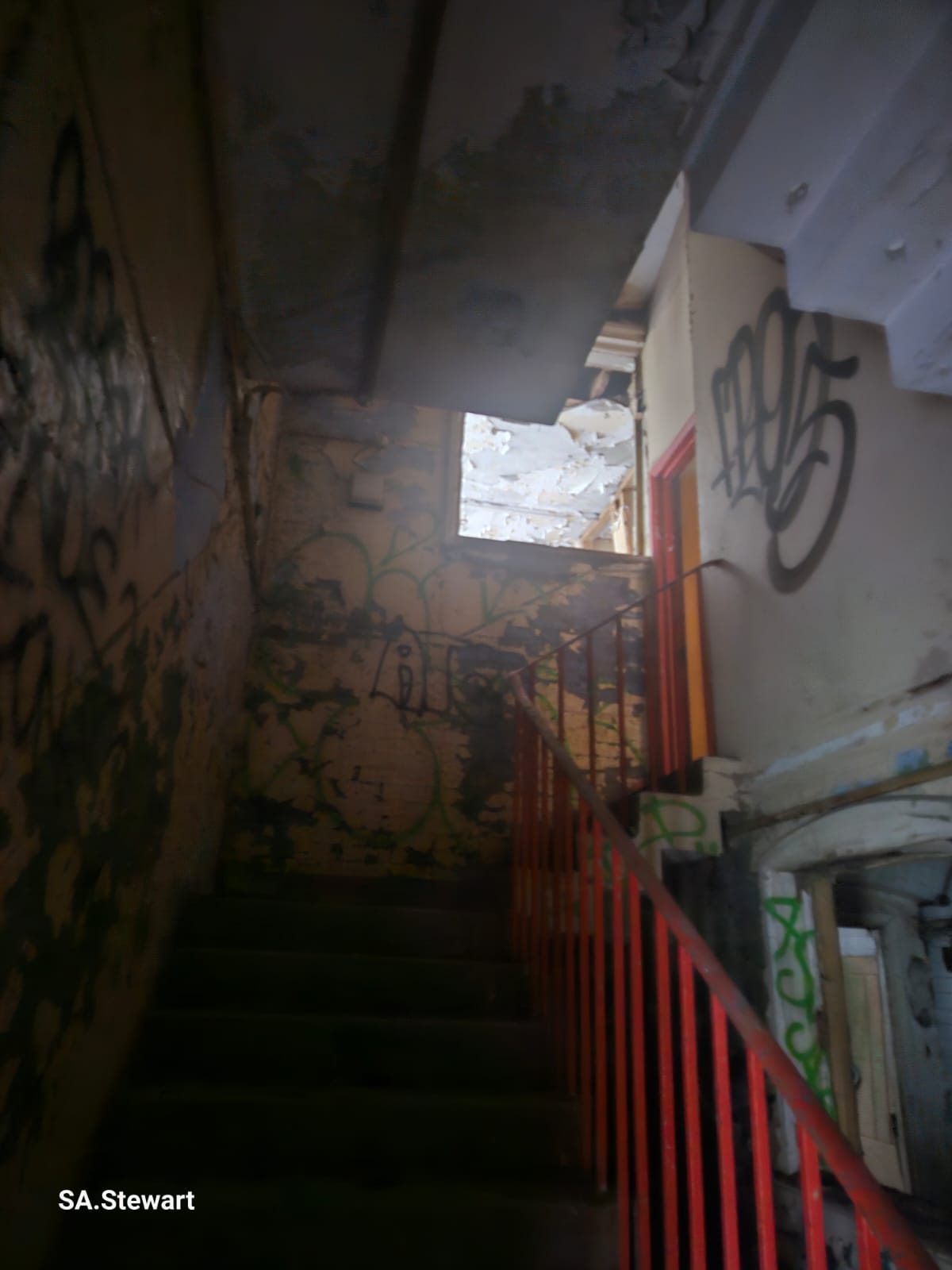 The interior stairwell, with its bright red industrial handrail and damaged ceiling