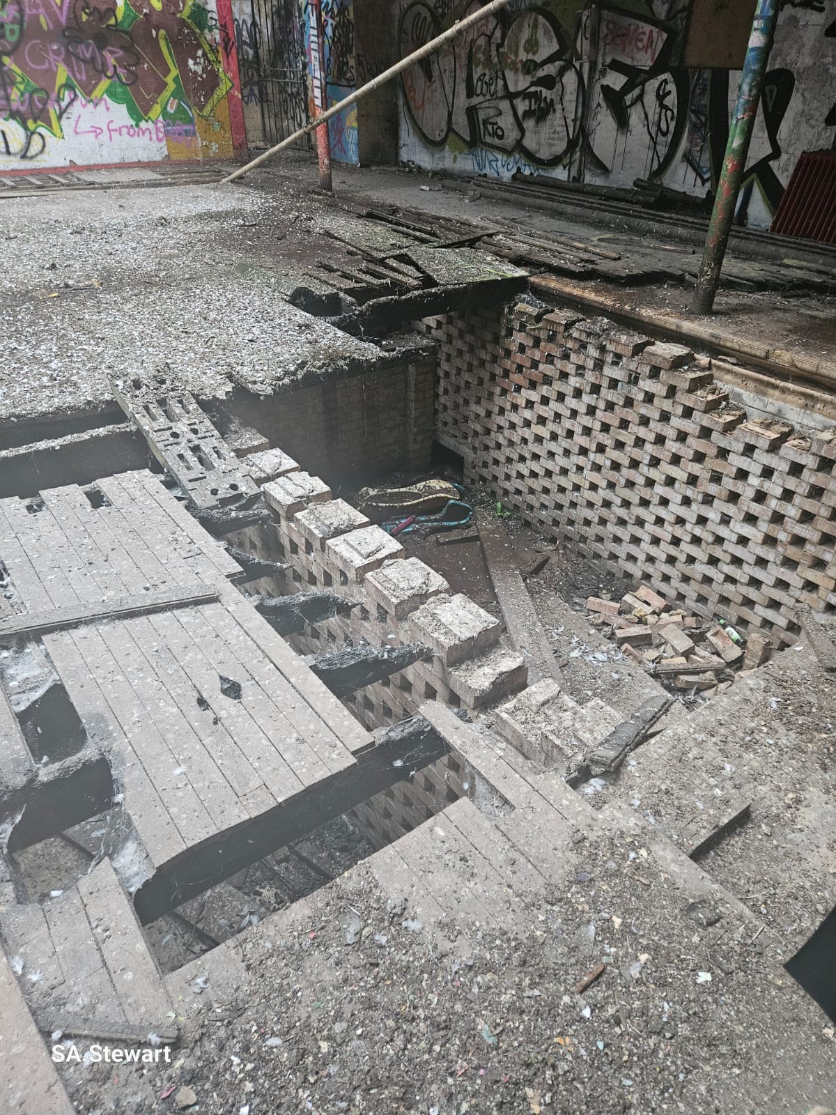 A partially collapsed floor section, revealing the historic honeycombed brick foundation