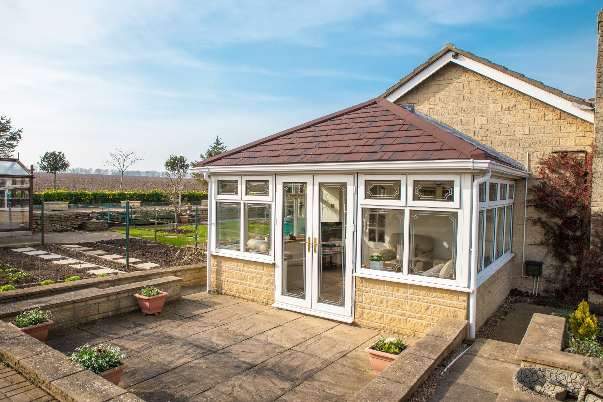 Conservatory with reddish-brown tiled roof on stone-effect dwarf wall
