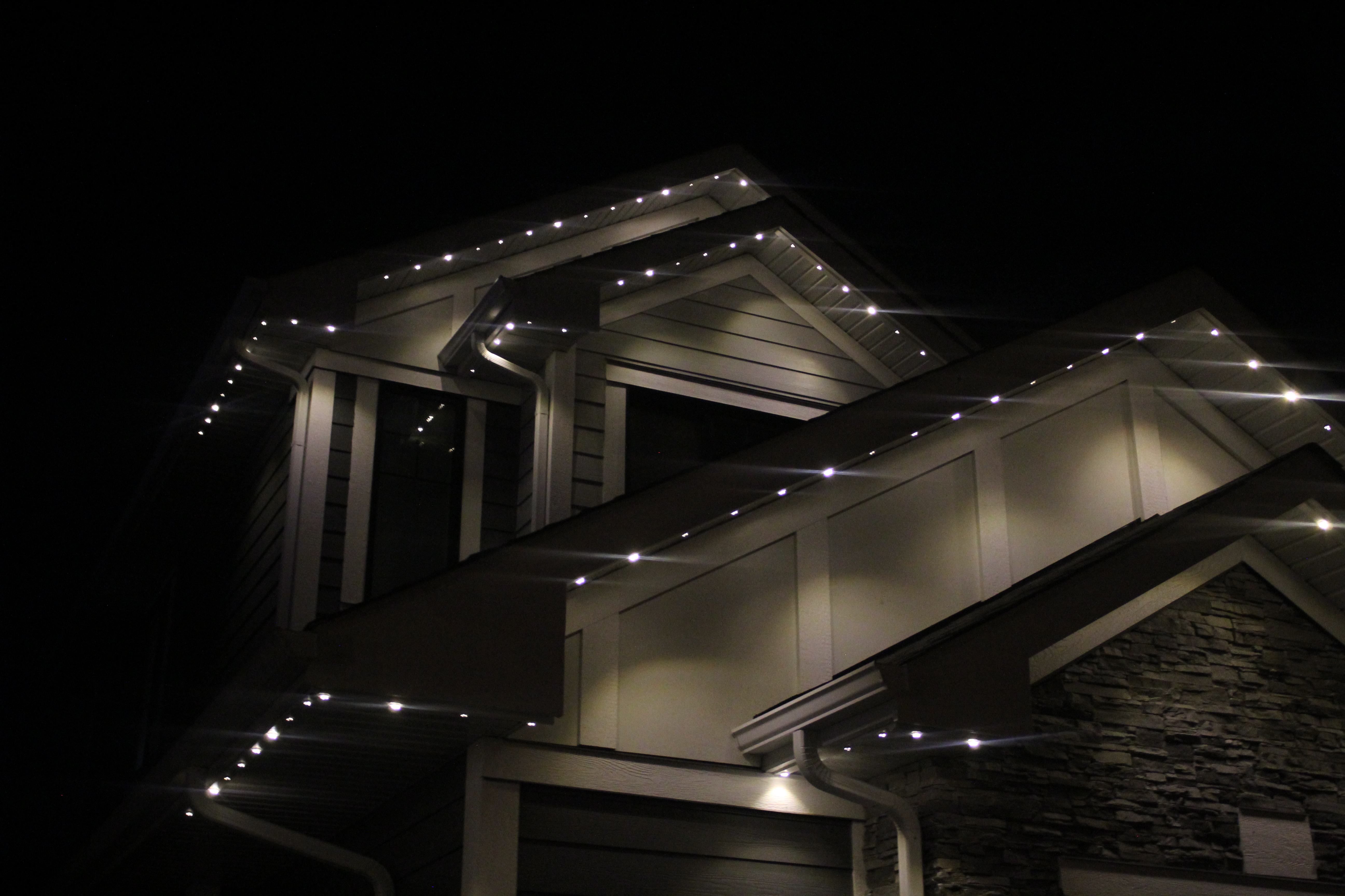 Night view of stacked rooflines with bright white permanent LED lights along eaves and gables