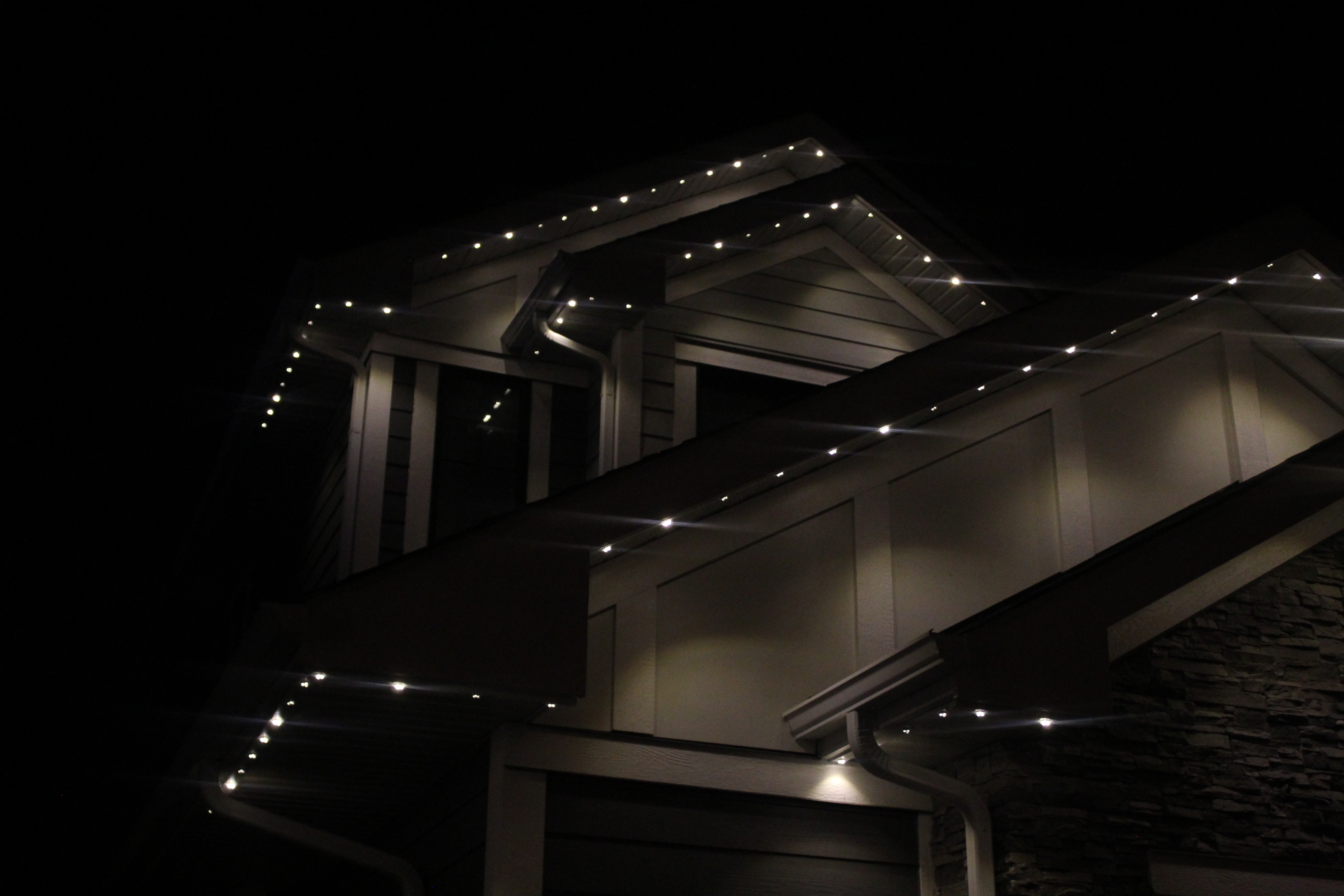 Warm white permanent LED lights tracing the eaves of a multi-level home at night