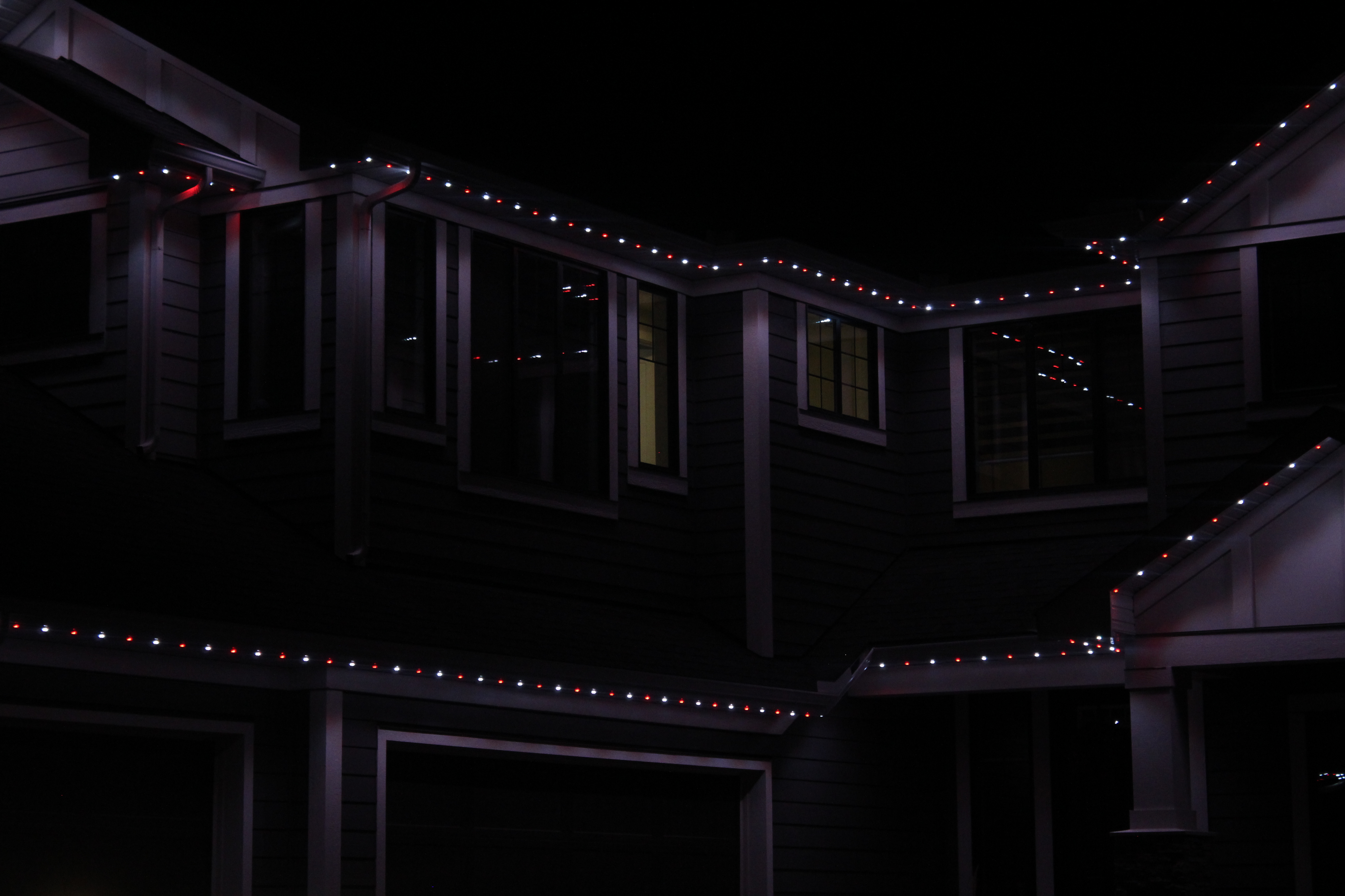Long runs of red and white permanent LED lights along the eaves of a two-story home