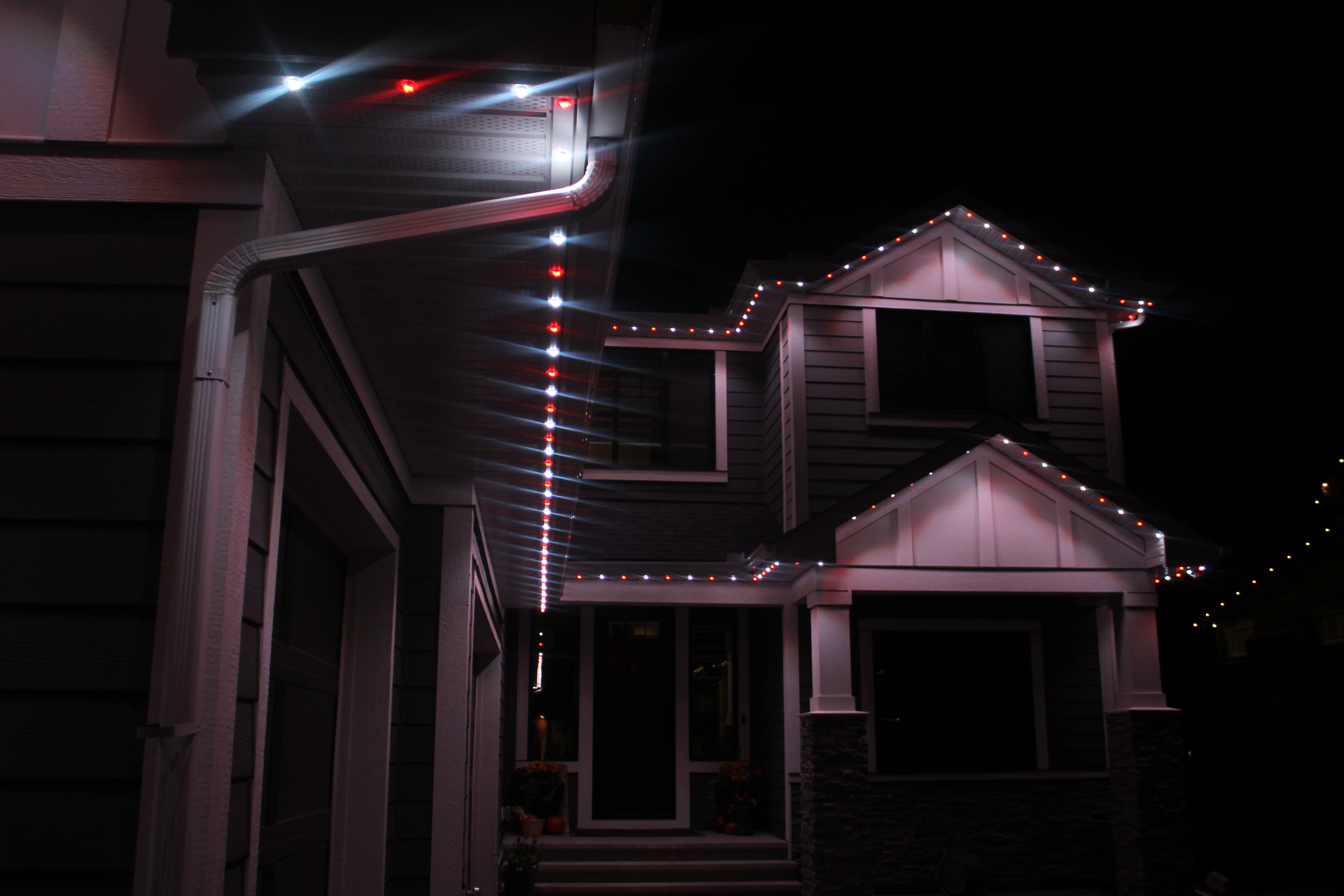 Red and white permanent LED soffit lights leading toward a home entrance at night