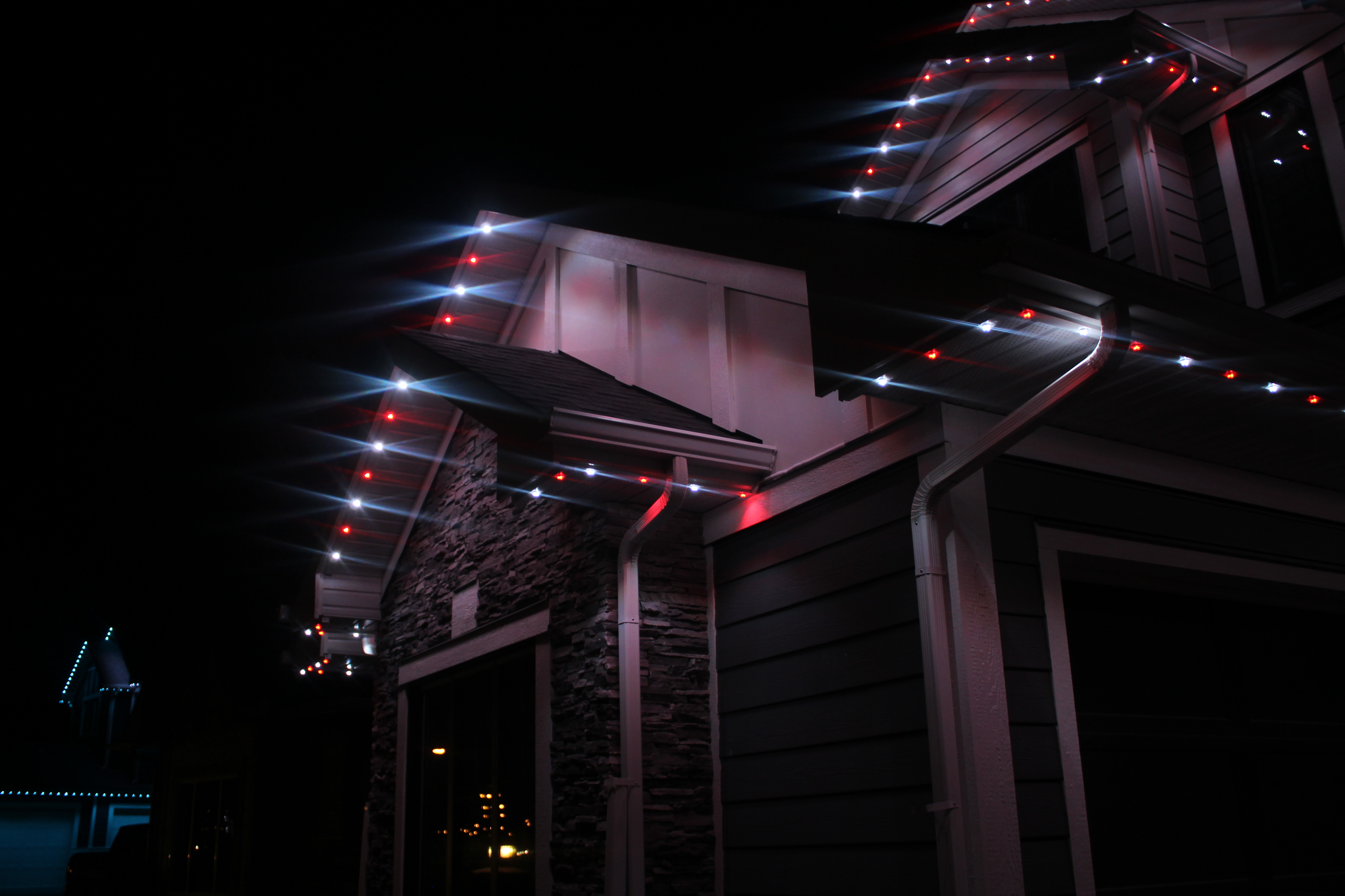 Close view of red and white permanent LED lights with starburst glow along rooflines and gutters