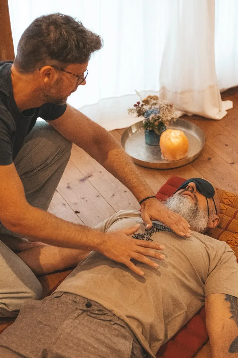 Breathwork-Einzelbegleitung: Jan Peters legt einem liegenden Klienten mit Augenmaske die Hände auf die Brust