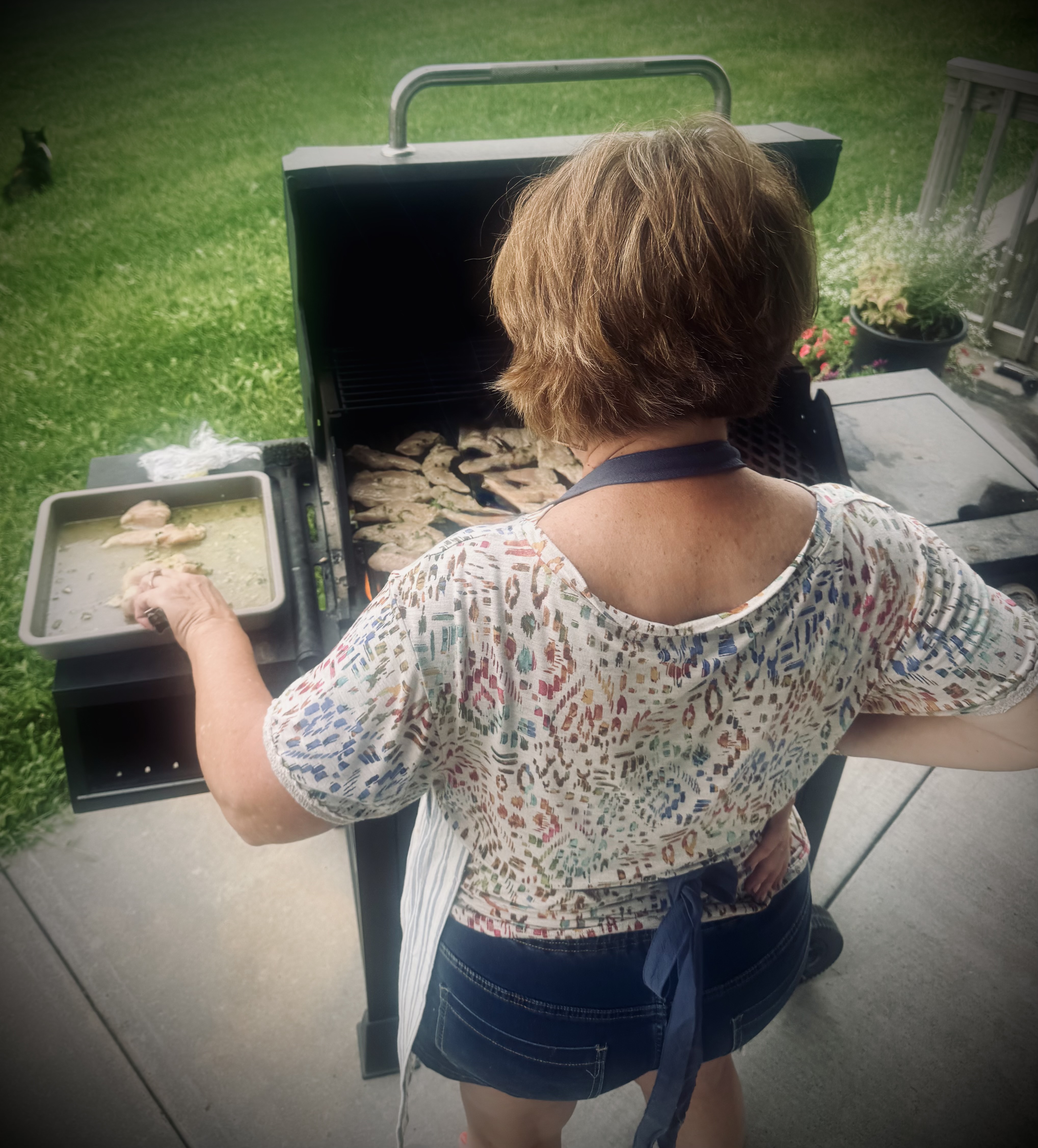 A woman grilling chicken outdoors on a patio