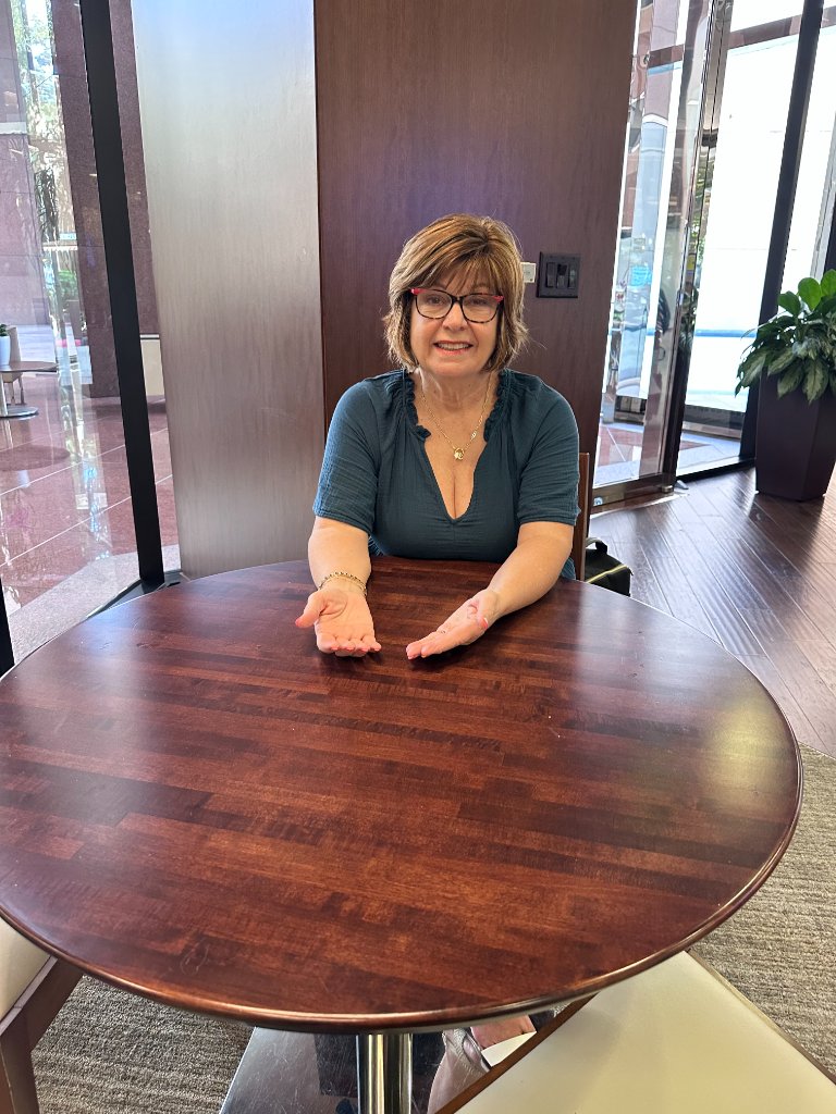 Lynette Sorrentino seated at a round wooden table, hands open in welcome