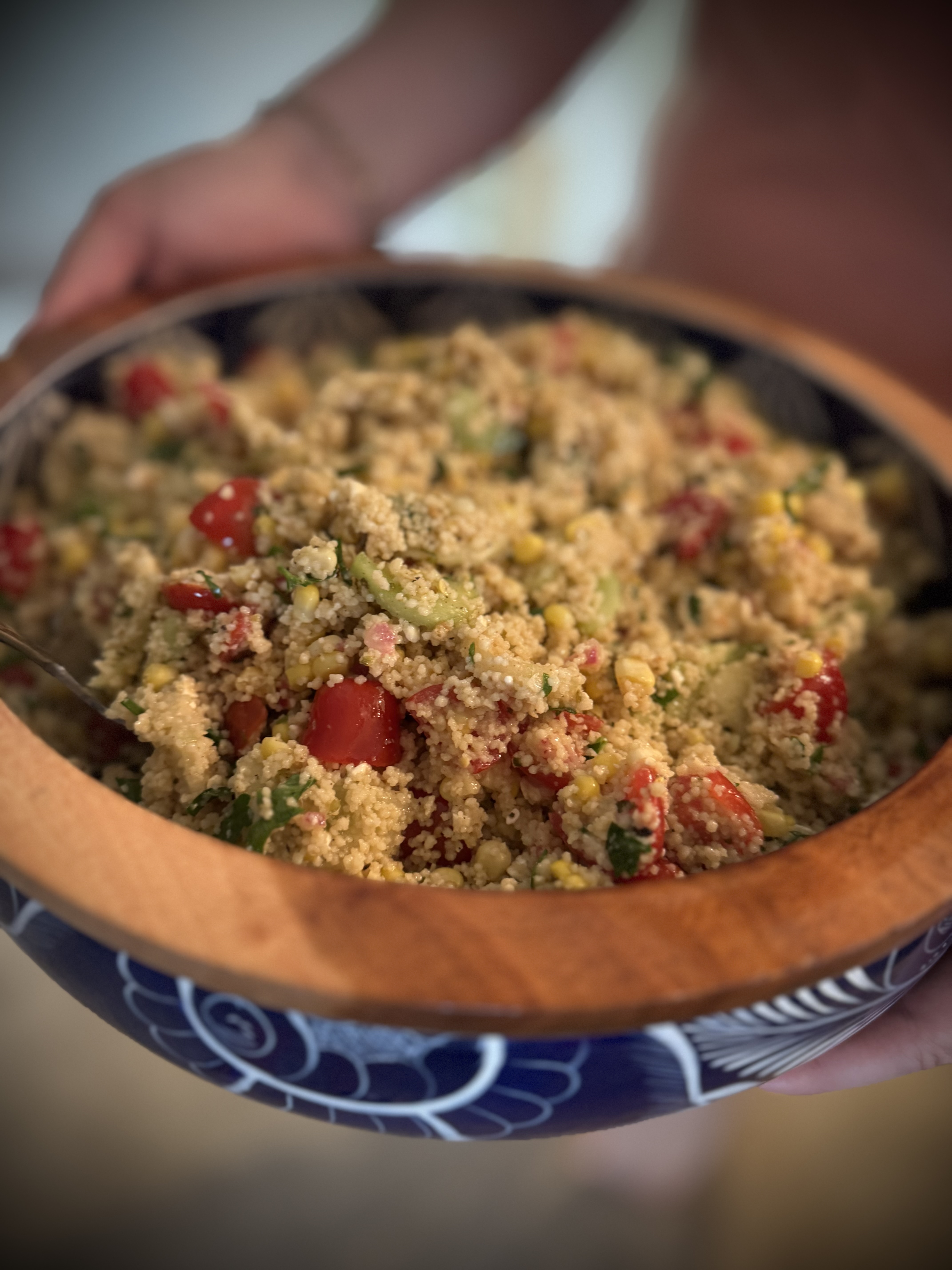 Hands holding a rustic bowl of couscous salad