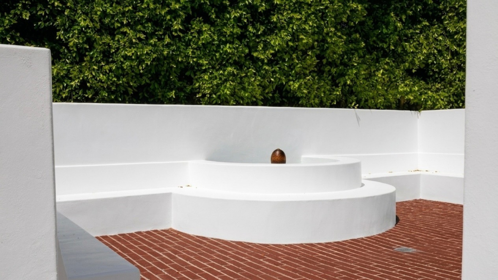 Curved plaster seating feature with brick paving and hedge backdrop.