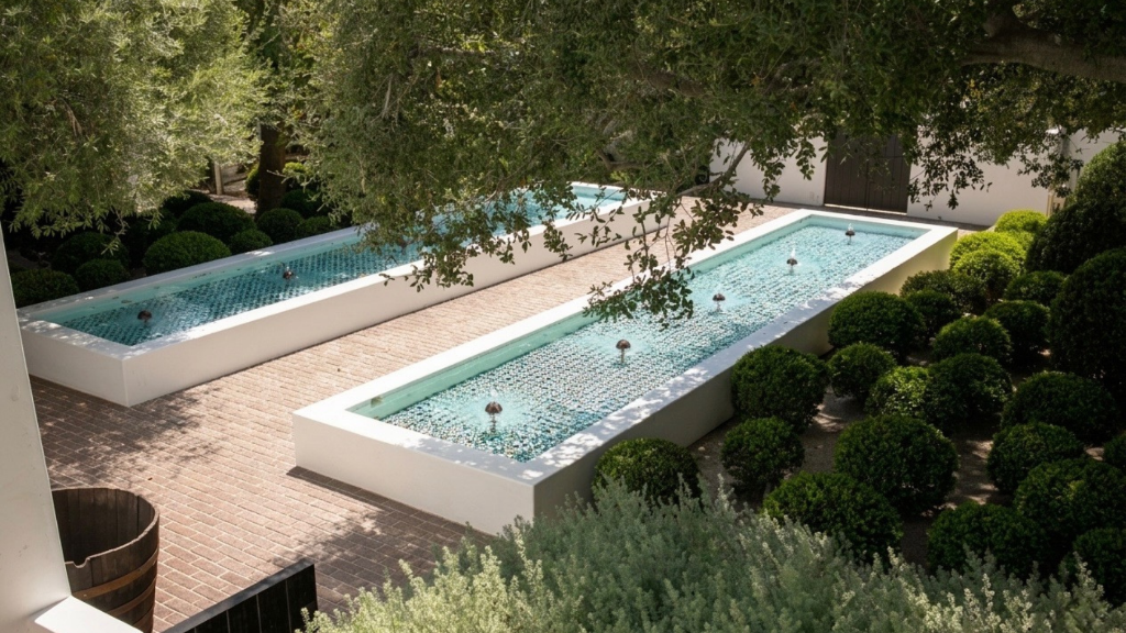 Aerial-angle reflecting pools with mosaic tile, boxwood spheres, and mature canopy