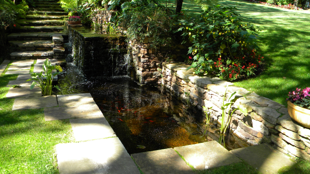 Koi pond with stone waterfall, flagstone surround, lawn panel, and perennial borders