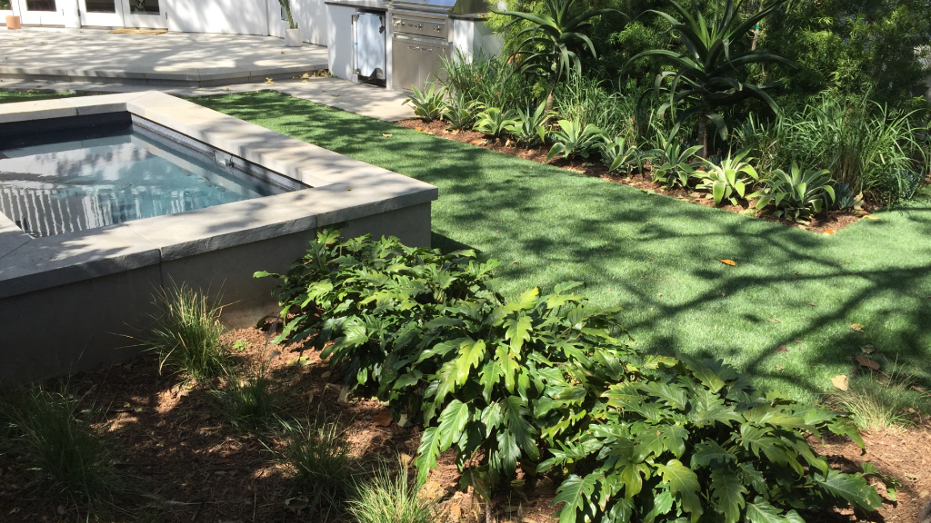 Raised concrete spa with tropical planting, synthetic lawn, and outdoor kitchen