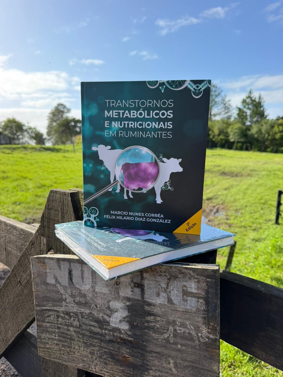 Exemplares do livro Transtornos Metabólicos e Nutricionais em Ruminantes, 2ª edição, apoiados em mourão de cerca no campo