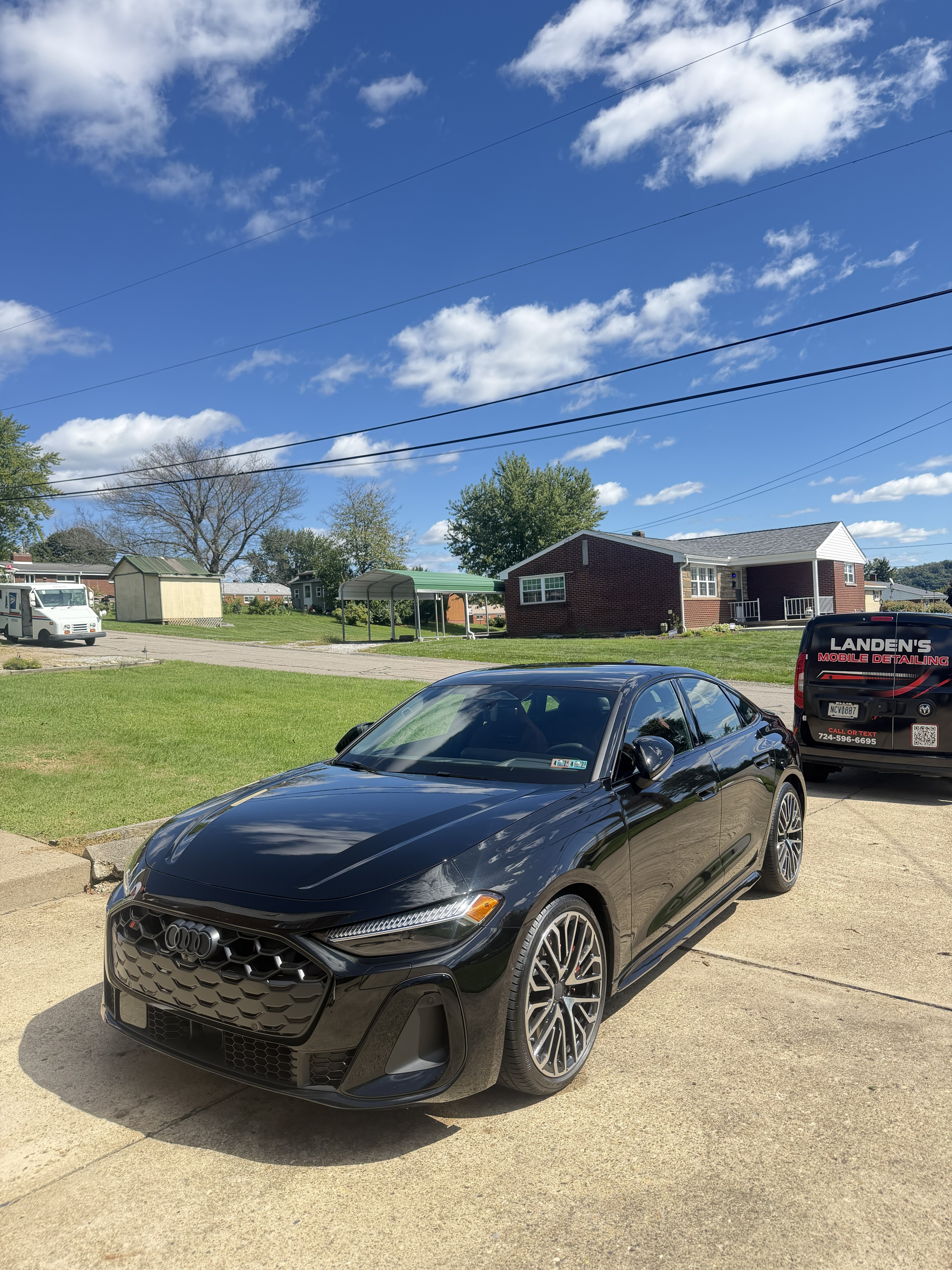 Glossy black Audi sedan full detail parked in a driveway with the Landen's Mobile Detailing van behind it
