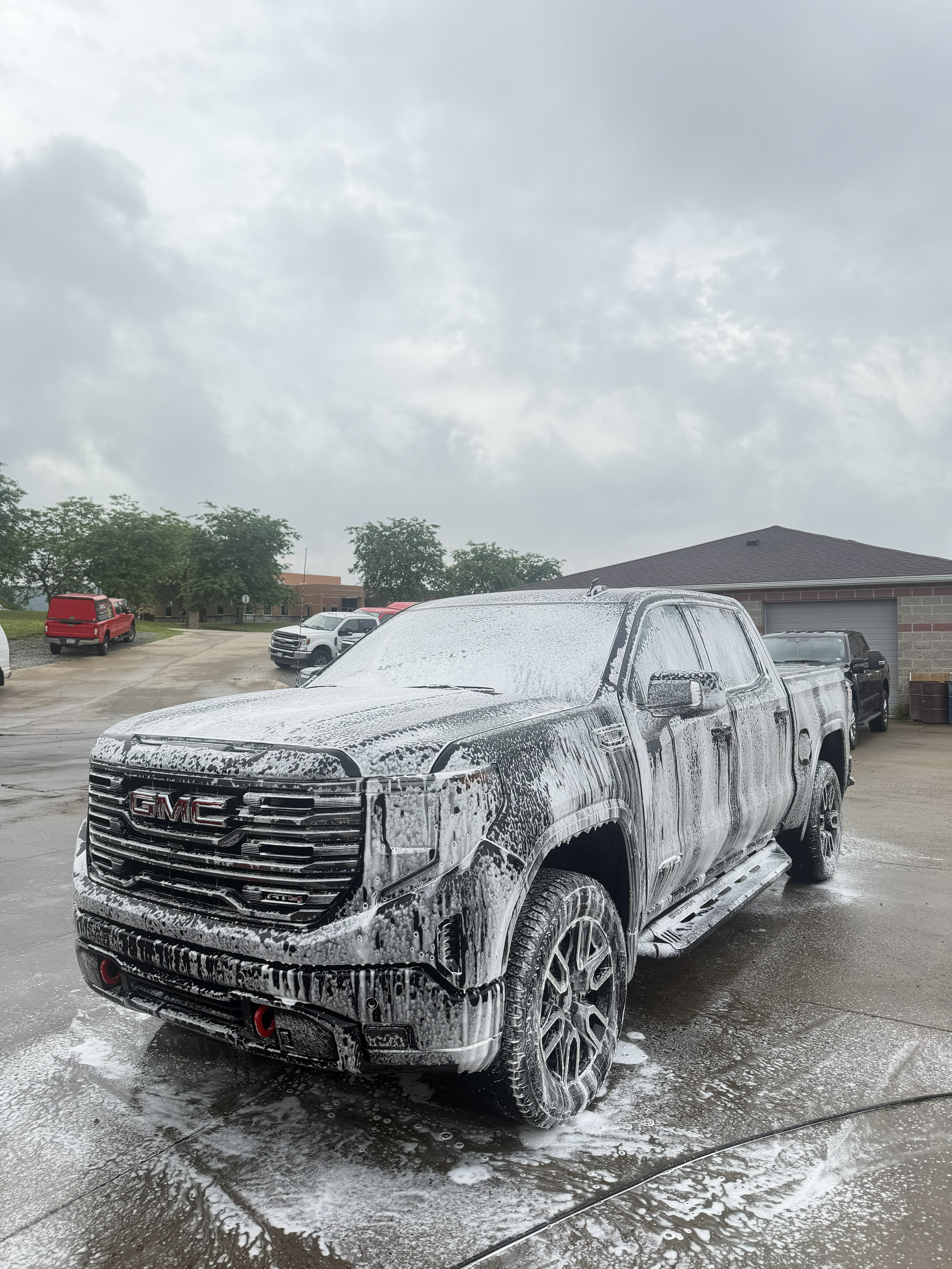 Dark GMC Sierra pickup truck covered in thick white snow foam during a mobile wash in Pittsburgh, PA