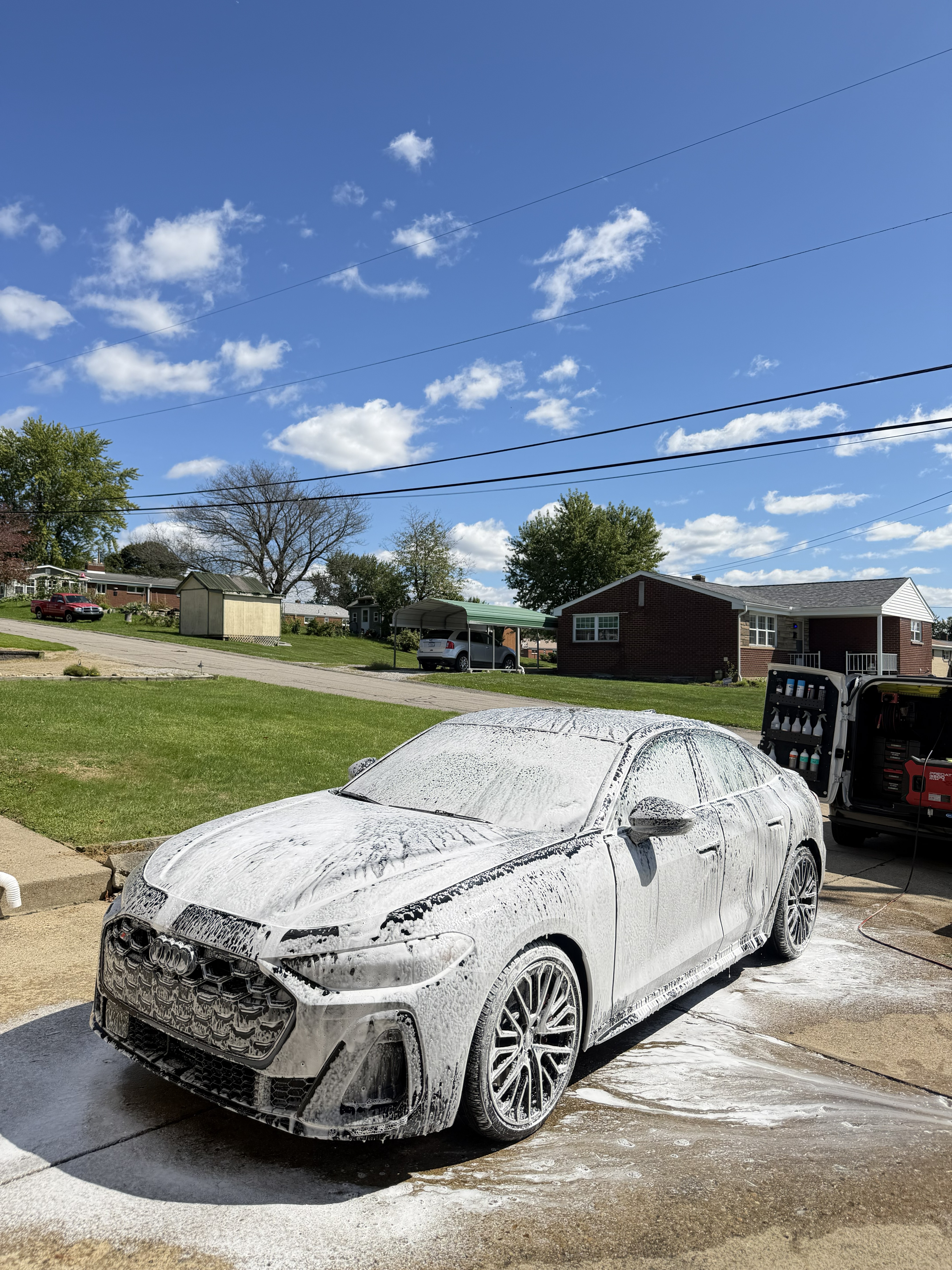White Audi S5 sedan covered in foam during a mobile detail on a driveway