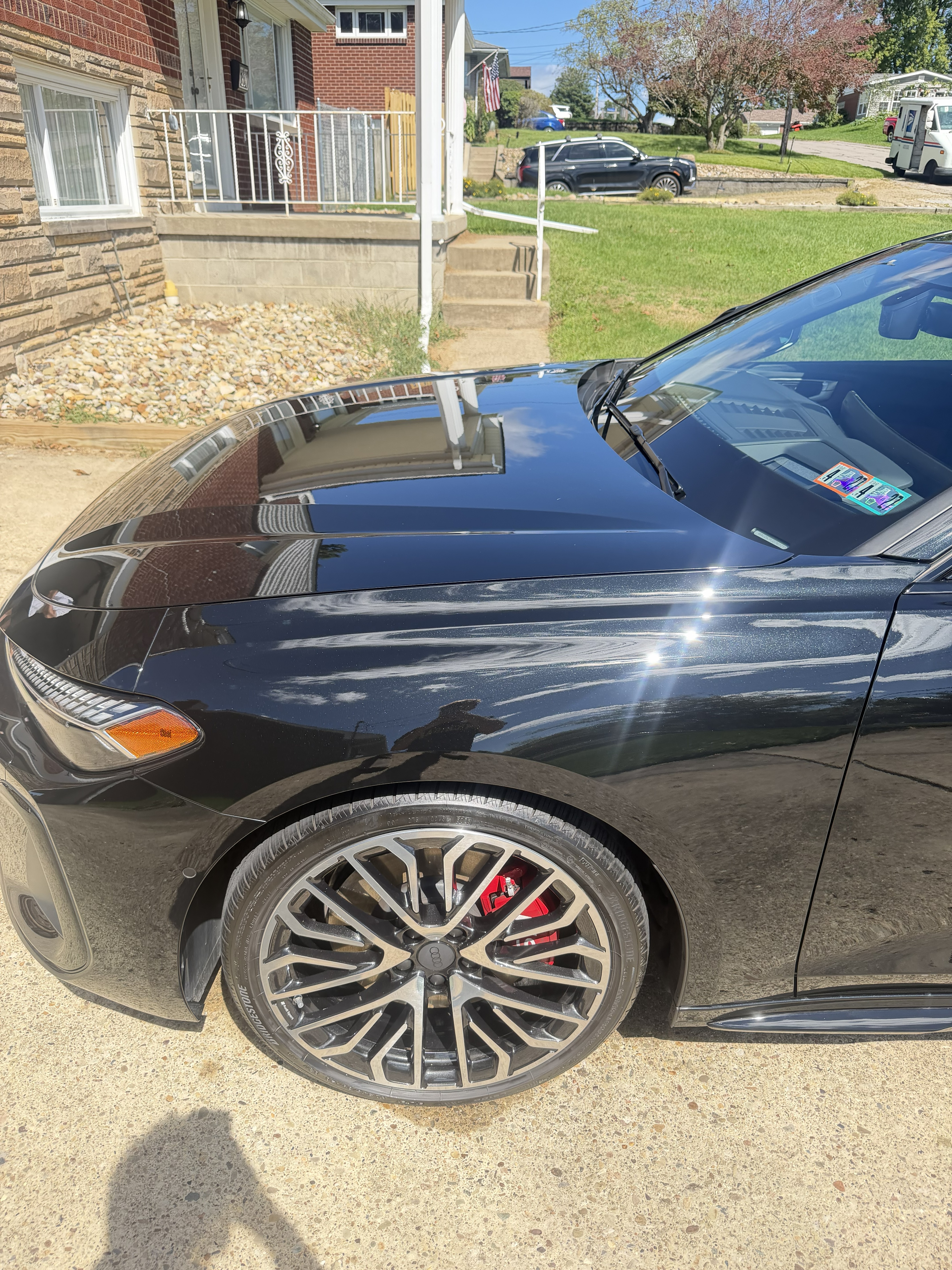Front left quarter of a glossy black Audi sedan showing multi-spoke wheels and red brake calipers after a mobile detail