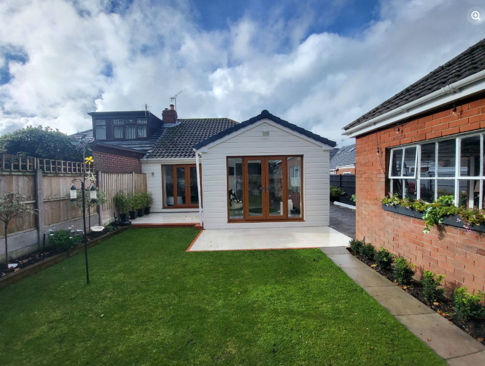 Completed rear extension with cream cladding and brown-framed French doors overlooking a garden in Billinge