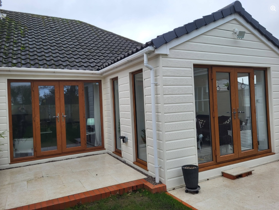 Close-up of the cream-clad extension with brown French doors opening onto a stone patio