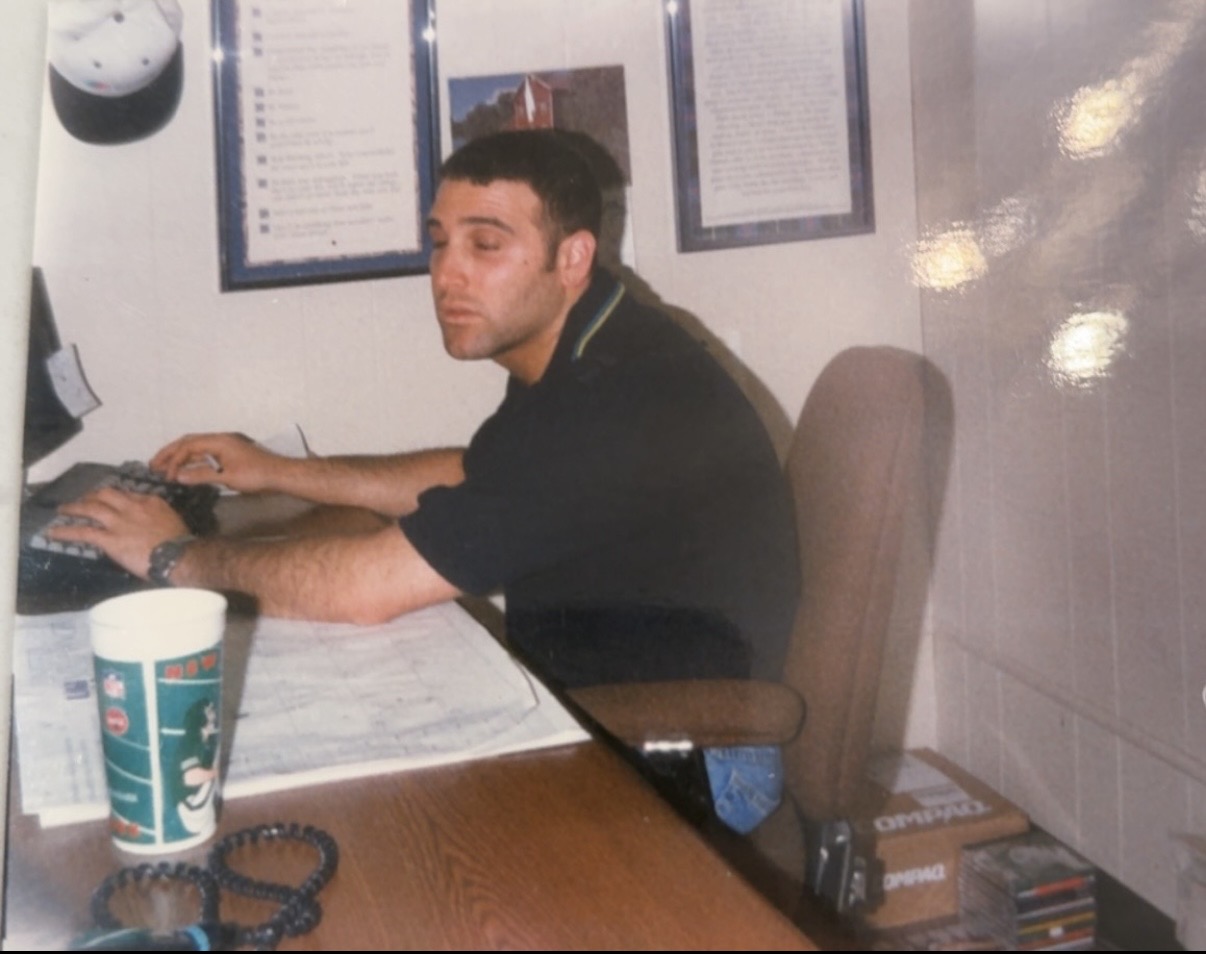 Family member working at a desk in a wood-paneled office surrounded by papers and a computer