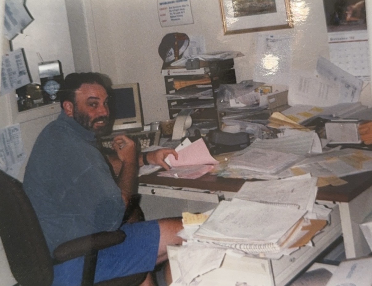 Better Pak team member working at a cluttered office desk covered in invoices and order forms