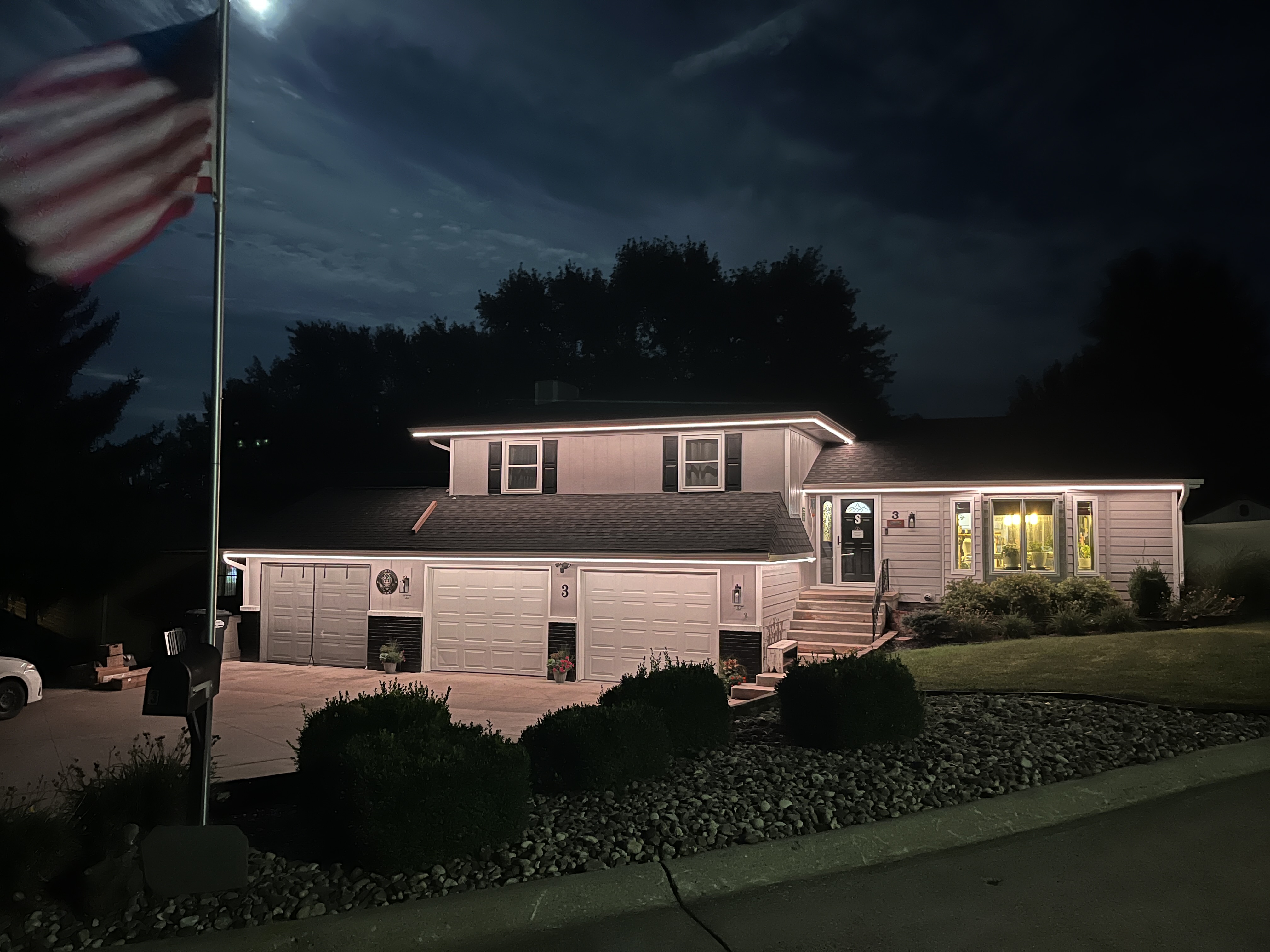 Home with a three-car garage illuminated by warm white permanent roofline lighting at night