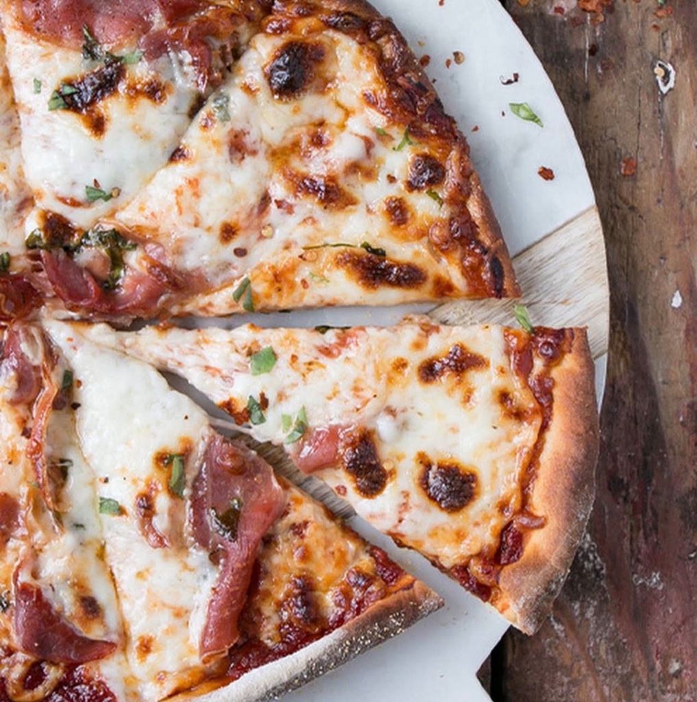 Pizza slices with prosciutto on wooden board