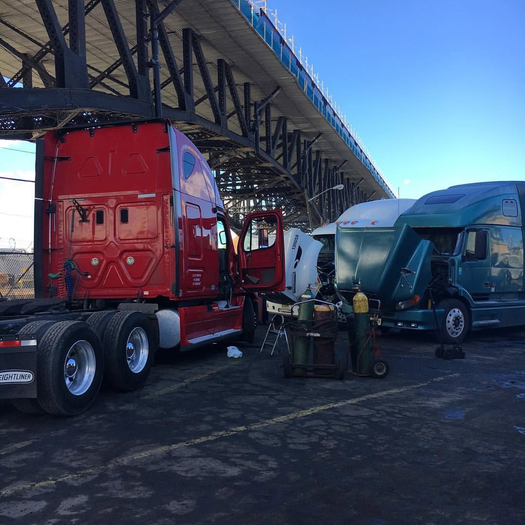 Red Freightliner tractor beside a truck with its hood tilted open