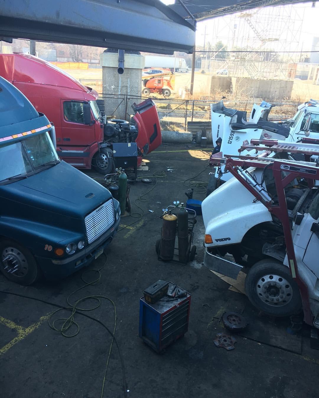 Teal and red tractors staged in the repair yard with welding cart