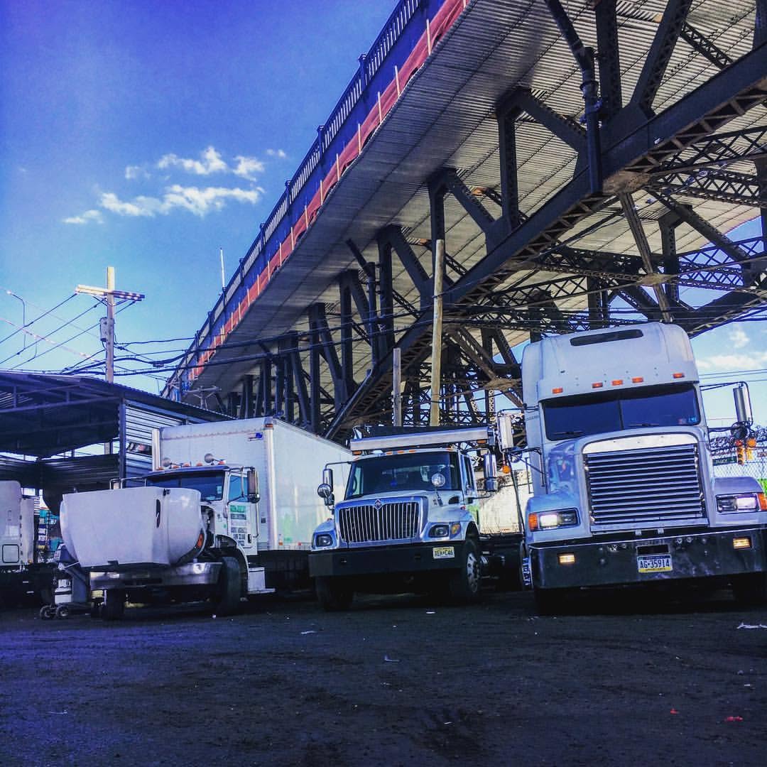 Three semi trucks parked beneath an elevated steel bridge