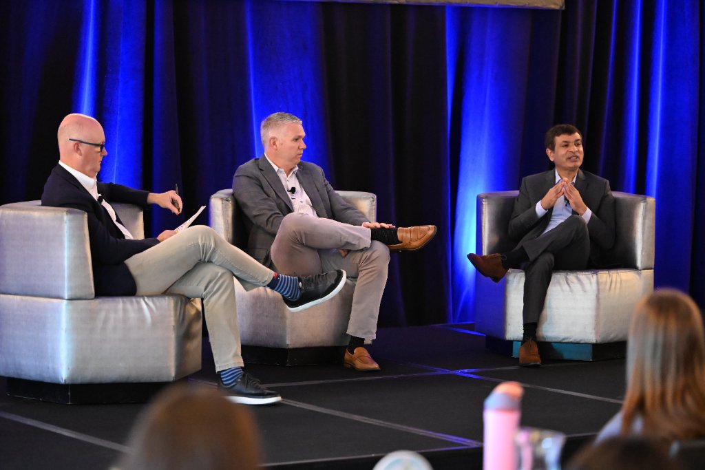 Three panelists seated on stage in discussion at a corporate event