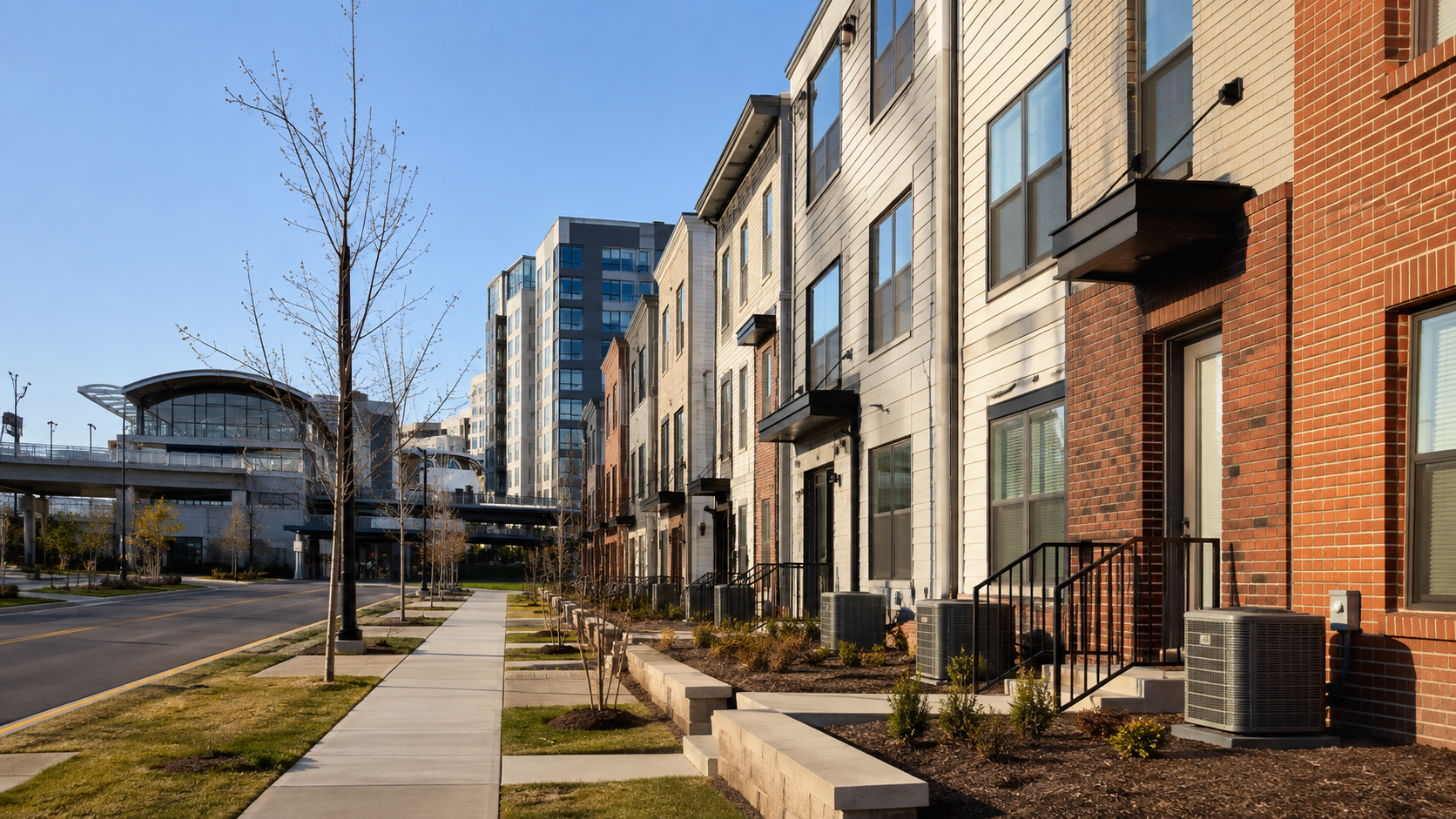 Perspective of contemporary Franconia townhomes with red brick and beige siding, HVAC condenser units, and a transit station in the background