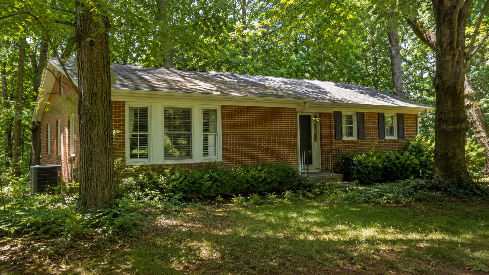 Red brick ranch-style house surrounded by mature trees with an HVAC condenser unit — attic insulation and HVAC blog post