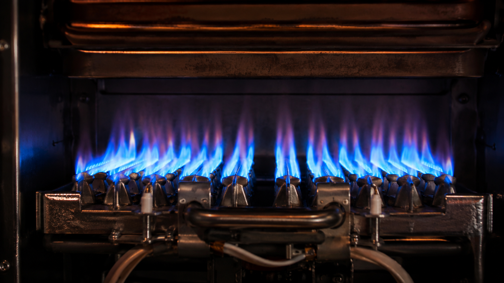 Close-up of a residential furnace burner assembly with clean blue flames rising from metallic burner heads in a dimly lit heat exchanger chamber