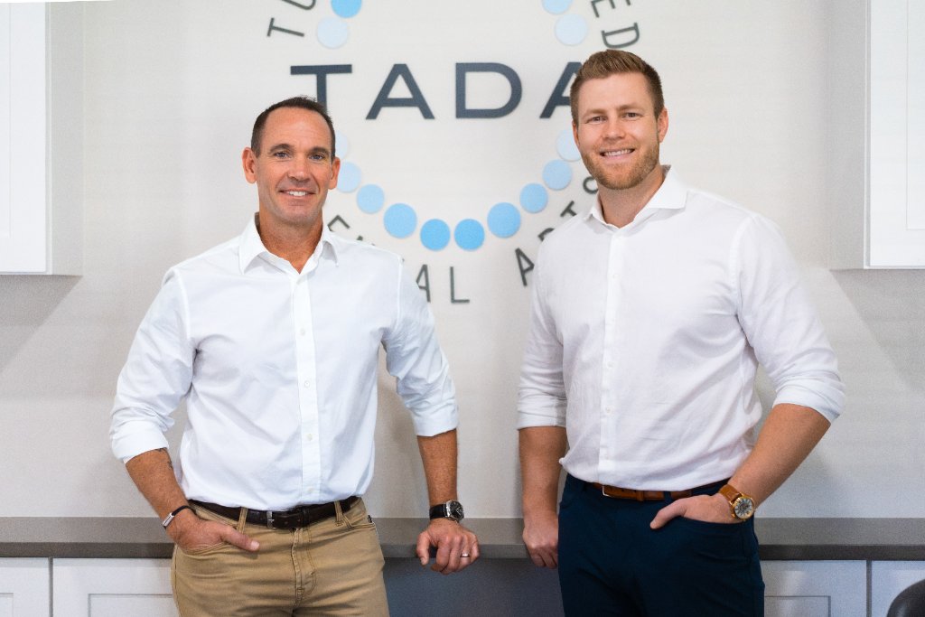 The TADA Dental doctors in front of the practice logo