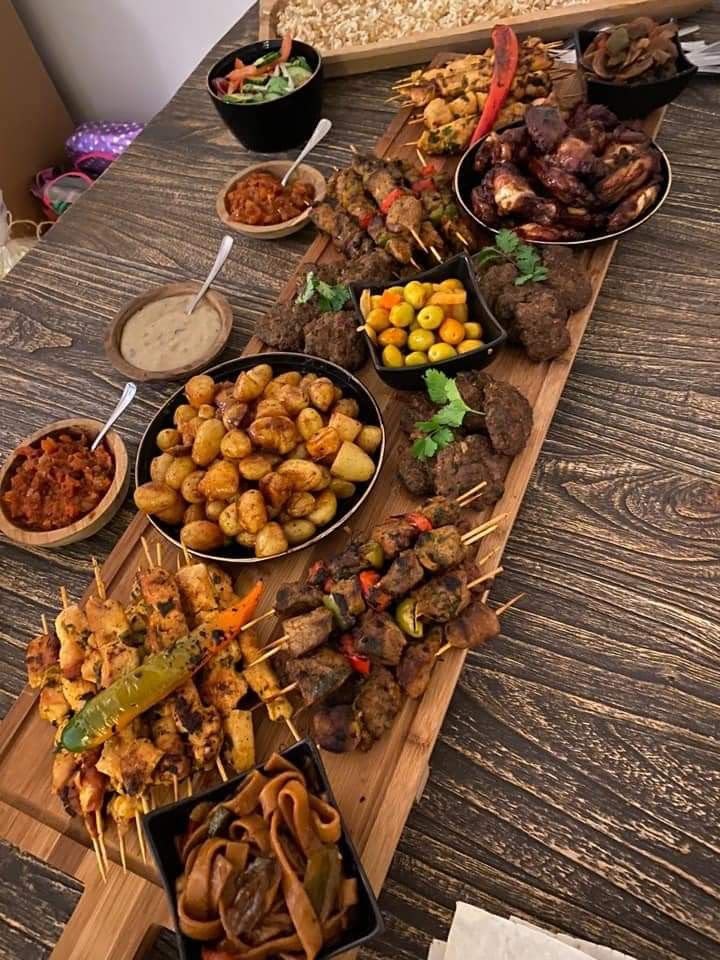 Large spread of skewers, potatoes, sauces on wooden board