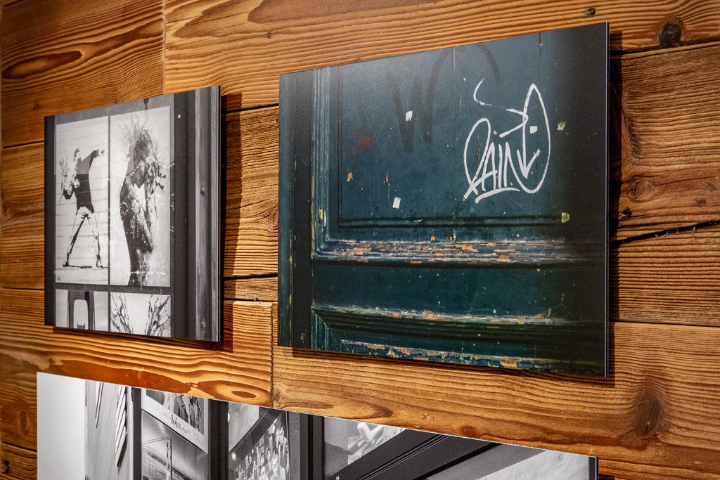 Zwei Kunstdrucke an Holzpaneelwand: Schwarz-weisse Architekturfotografie und Tuer mit Graffiti